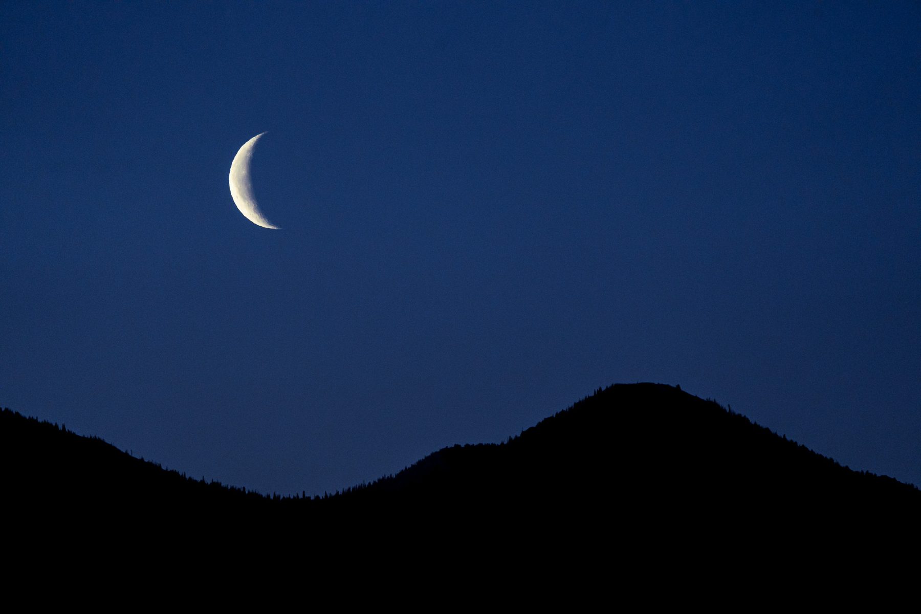 A crescent moon above a dark mountain silhouette