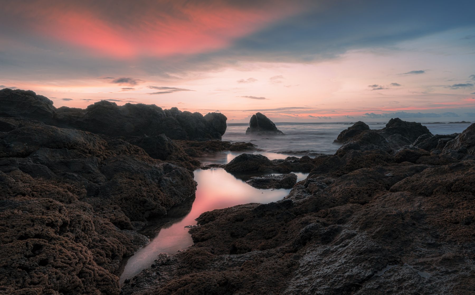 A tidal channel curving through dark coastal rock under a pink sunset