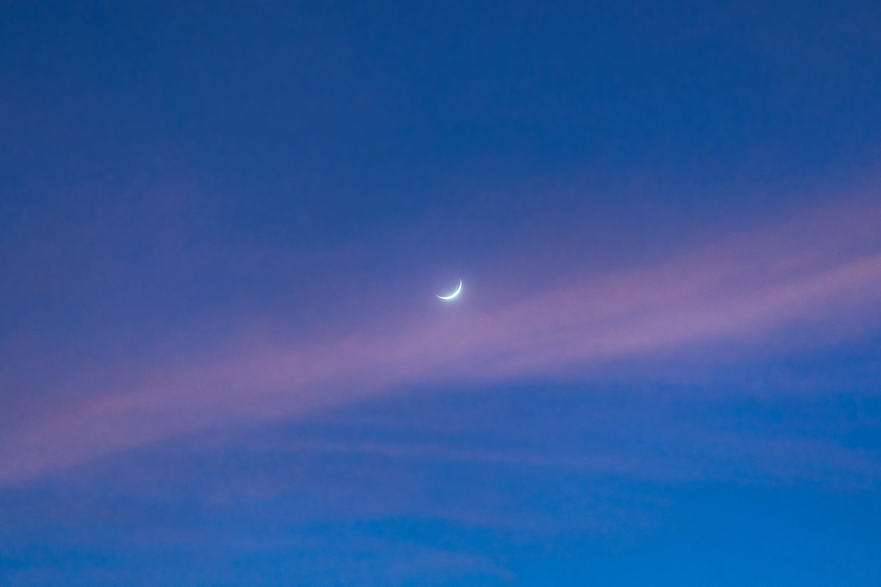 A waxing crescent moon in a deep blue evening sky