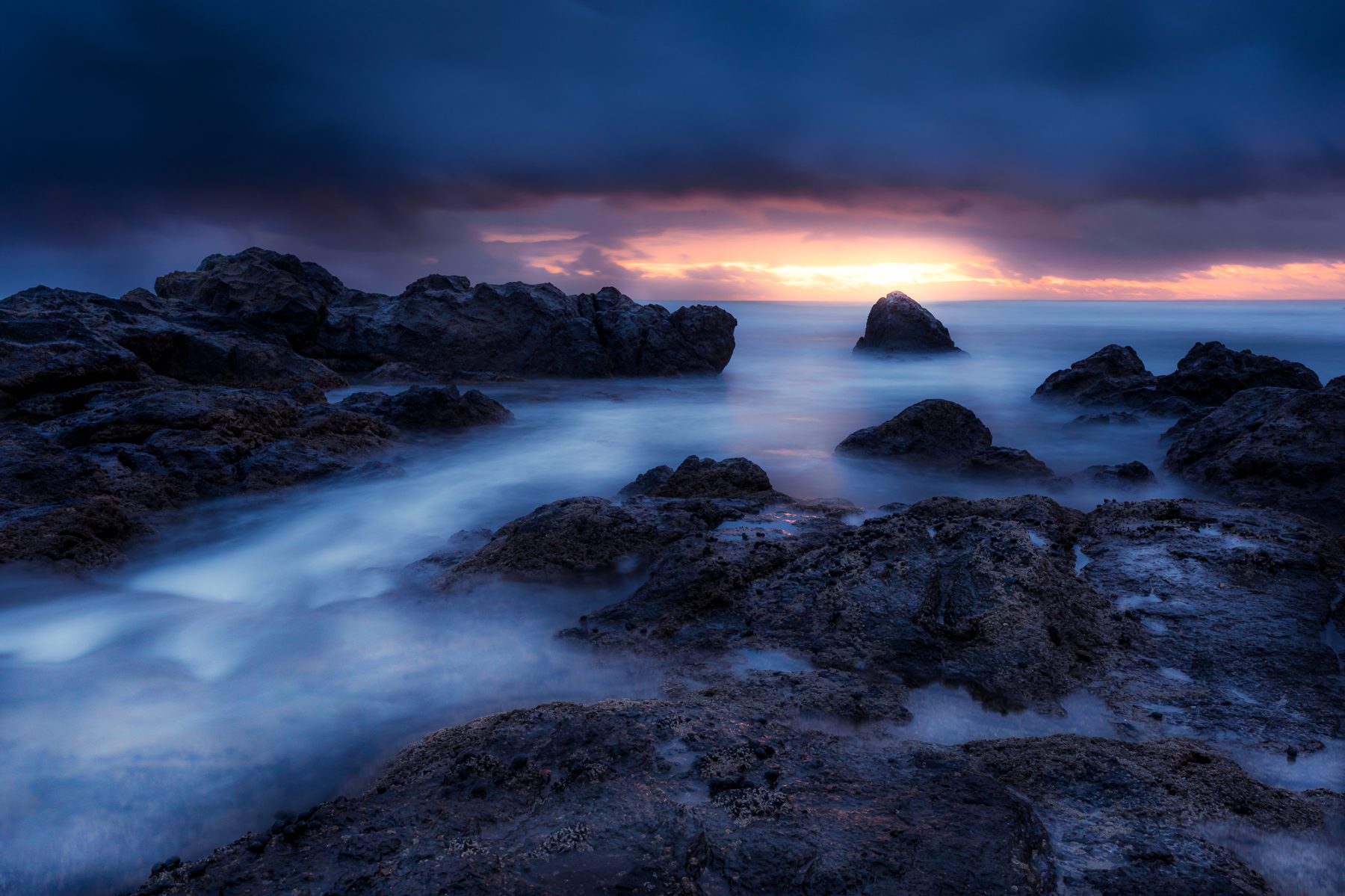 Long exposure of surf drawn out in white trails around a sea stack at blue hour